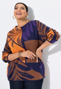 Haut en tricot coloré mettant en vedette un motif de feuilles orange et violet sur un fond marron. Épaules tombantes et coupe décontractée.