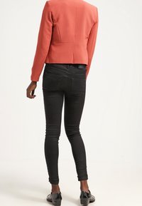 Blazer corail ajusté avec un design structuré et une fente à l'arrière, associé à un jean skinny noir, présentant un tissu lisse et une coupe longueur cheville.