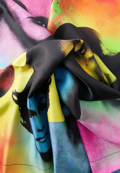 Μεταξωτό ύφασμα με πολύχρωμα ποπ αρτ σχέδια πολλαπλών γυναικείων προσώπων σε αποχρώσεις του μπλε, κίτρινου, ροζ και πορτοκαλί, παρουσιάζοντας πτυχώσεις και υφή.