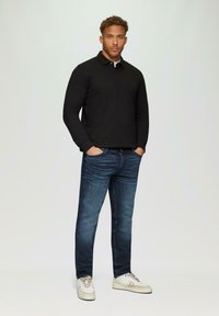 Polo shirt à manches longues noir, jean bleu foncé avec un léger délavage et baskets beiges. Design simple et coupe décontractée.