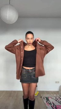 Ženska z zada zvezanimi lasmi nosi rjav flis preko črnega kratkega topa, črno denim mini krilo in črne škornje do kolen v zaprtih prostorih.