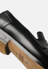 Scarpa in pelle nera con un design elegante, punta affusolata e suola in gomma resistente. Presenta dettagli di cucitura e un marchio impresso sulla suola.