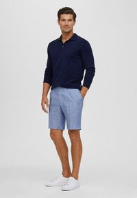 Polo a maniche lunghe blu navy, pantaloni corti azzurri in un tessuto testurizzato, abbinati a sneakers bianche. Design semplice e pulito, vestibilità classica.