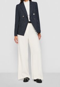 Marinblå dubbelknäppt kavaj med glänsande silverknappar, i kombination med högmidjade vita vida byxor. Texturerad tyg och strukturerad design.