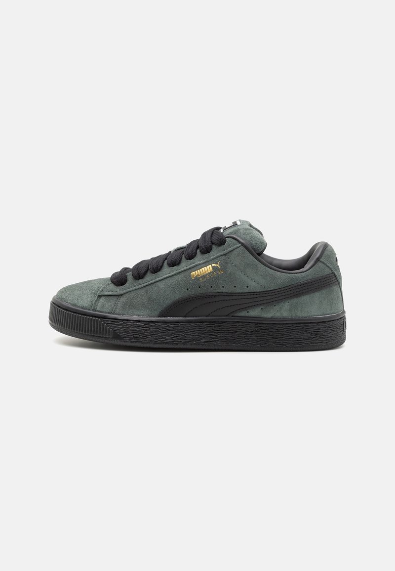 Baskets Puma en daim vert foncé avec semelle noire, lacets et bande latérale, présentées de profil sur un fond gris clair.