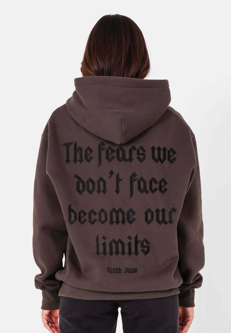 Sweat à capuche marron foncé avec un grand texte noir au dos. Doté de poignets et d'un ourlet côtelés, d'une texture douce et d'une coupe décontractée.