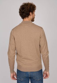 Pull en maille en doux tissu beige avec un col haut, des poignets et un ourlet côtelés, présentant un design simple et épuré. Texture agréable.