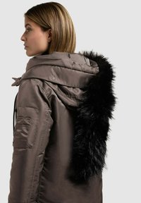 Brun isoleret jakke med en aftagelig sort faux fur hættekant, der har lynlåslukning og sidelommer. Blød, glat tekstur.