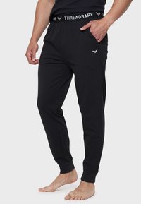 Schwarze Baumwoll-Jogginghosen mit elastischem Bund, die mit "THREADBARE"-Branding, Seitentaschen und schmal zulaufenden Bündchen ausgestattet sind. Glatte Textur.