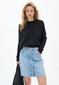 Črna pletena majica z dolgimi rokavi v kombinaciji s svetlo modrim jeans krilom, ki ima sprednji gumbni trak in stranske žepke.