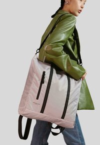 Borsa tote in nylon di colore rosa chiaro con cerniere e manici neri, caratterizzata da una superficie texture e cuciture diagonali. Indossata a tracolla.