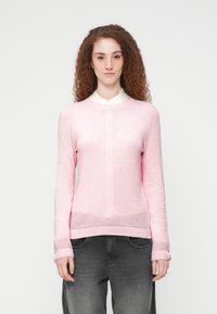 Ανοιχτό ροζ πλεκτό πουλόβερ με υφασμένο σχέδιο, στρογγυλή λαιμόκοψη και ριμπ μανσέτες, σε συνδυασμό με σκούρο γκρι τζιν.