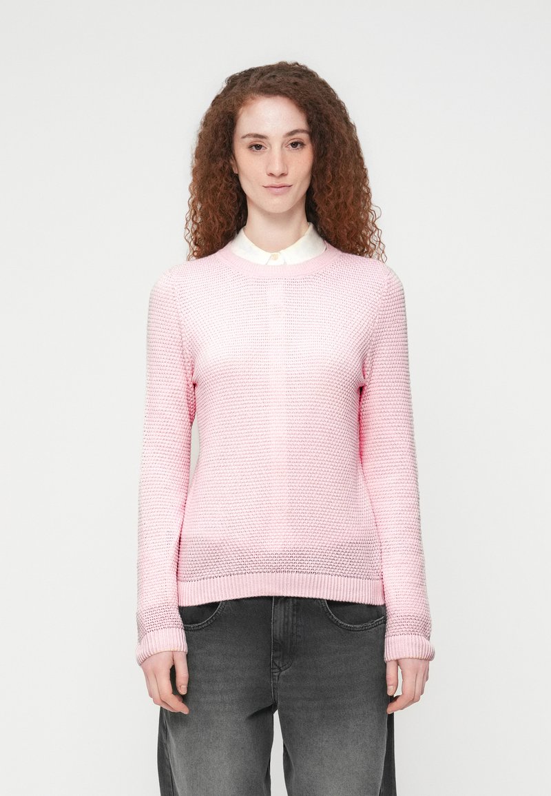 Ανοιχτό ροζ πλεκτό πουλόβερ με υφασμένο σχέδιο, στρογγυλή λαιμόκοψη και ριμπ μανσέτες, σε συνδυασμό με σκούρο γκρι τζιν.