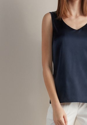Top maniche senza con scollo a V in satin blu navy con vestibilità rilassata. La texture liscia e le fessure laterali aumentano il comfort e lo stile.