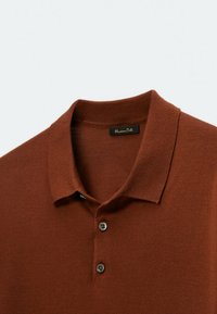 Brown polo shirt featuring a collared neck, short sleeves, and two black buttons on the placket. Made from a soft, textured material.