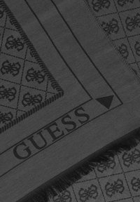 Écharpe noire avec un motif texturé mettant en avant des détails en relief et un bord à franges. Logo "GUESS" embouti le long d'un bord.