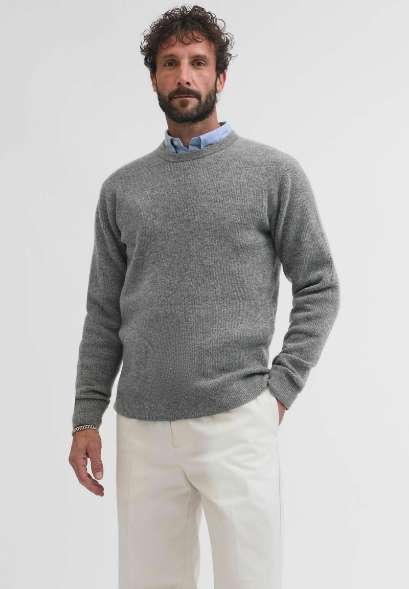 Maglione grigio a maglia con collo rotondo, maniche lunghe e polsini a costine, abbinato a pantaloni beige. Il tessuto sembra morbido e strutturato.