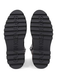 Černé podešve z gumy s hlubokými drážkami, s vyraženým nápisem "CALVIN KLEIN JEANS". Texturované pro lepší přilnavost, s kulatou špičkou.