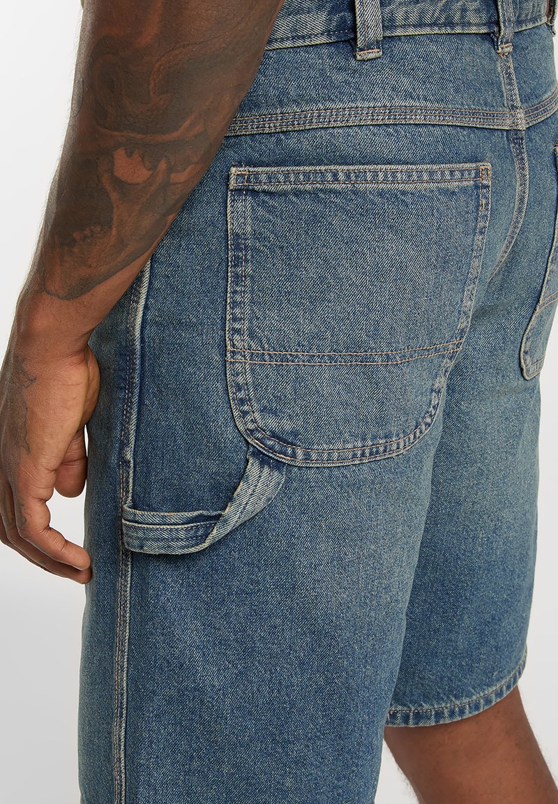 Shorts di jeans in blu medio con una finitura strutturata, dotati di tasca laterale, tasca applicata sul retro e cuciture a contrasto.