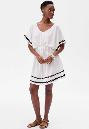 Witte jurk met een V-hals, een taille die is geaccentueerd, en korte mouwen. Zwart zigzag trim aan de mouwen en de zoom. Lichtgewicht stof.