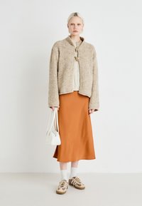 Beige teksturert strikket jakke, lys kremfarget topp, rustrød silkeskjørt, hvit veske, hvite sokker og beige-brune sneakers.