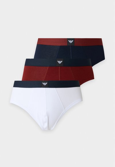 Trois slips pour hommes en blanc, rouge foncé et bleu marine, chacun avec une ceinture contrastante et un logo centré sur la bande.
