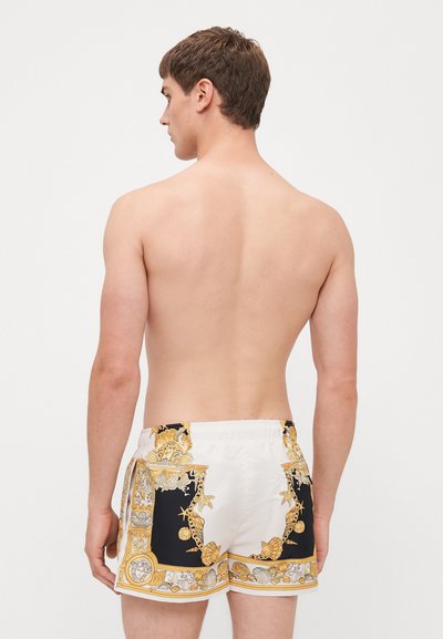 Shorts de bain pour hommes présentant un design noir et blanc avec des motifs de coquillages et de chaînes dorées, fabriqués en tissu lisse et léger, avec une taille élastique.