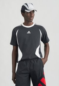 Svartvit sport-t-shirt med välvda vita detaljer och Adidas-logotyp. Matchas med svarta shorts med röda diagonala ränder.