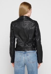 Zwart leren motorjack met gequiltte schouder- en elleboogdetails, slim fit en tailleverstellers, gecombineerd met lichtblauwe jeans.