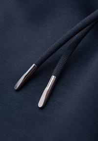 Gros plan sur un tissu bleu marine avec deux cordons sombres se terminant par des embouts métalliques argentés brillants.