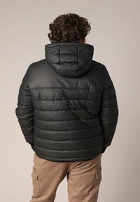 Doudoune noire avec capuche, présentant un design matelassé et des coutures horizontales. Portée avec un pantalon cargo beige.