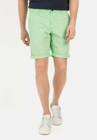Lichtgroene katoenen shorts met omgeslagen mouwen, voorzien van een knoopsluiting en riemlussen, gecombineerd met witte sneakers. Eenvoudig, casual ontwerp.