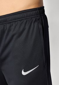 Sorte atletiske shorts lavet af glat stof med elastisk talje og sidelommer. Har et hvidt Nike swoosh-logo nederst til venstre.