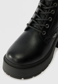 Μαύρο δερμάτινο μποτάκι έως τον ασ ankle με στρογγυλή μύτη, σχέδιο με κορδόνια, παχύ πάτο και υφές. Διαθέτει μεταλλικά μάτια και λεπτομέρεια λογότυπου.