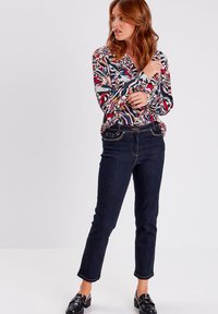 Multikleurige blouse met abstracte patronen; donkerblauwe denim jeans met slim fit; zwarte instappers; gladde texturen en contrasterende stiksels.