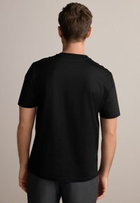 Camiseta negra de manga corta con cuello redondo. Tela de algodón suave, corte relajado y sin patrones ni adornos visibles.