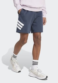 Navy blue sweat shorts with white stripes on the left side, featuring a smooth texture and an elastic waistband. White and black sneakers worn.
