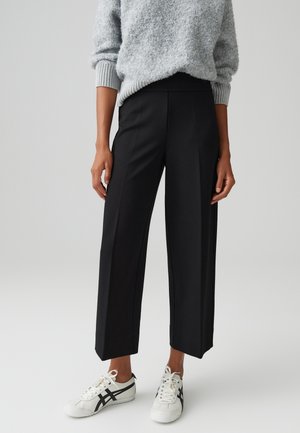 Zwarte wijde broek met hoge taille, met een gladde textuur en plooien aan de voorkant, gecombineerd met witte sneakers en een lichtgrijze trui.