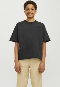 Svart oversized t-shirt med kort ärm och rund halsringning, med präglad logotyp på framsidan. Kombinerad med ljusa beige linnebyxor.