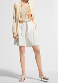 Blazer i lys gul linned, blomstret top i pastelfarver, hvide skræddersyede shorts og hvide hæl sandaler.