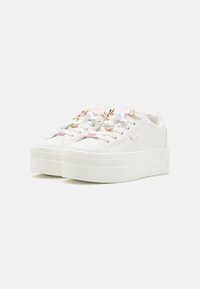 Baskets à plateforme blanches avec une finition lisse, ornées de breloques de lacets multicolores et d'une semelle en caoutchouc texturée avec des rayures verticales.