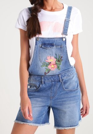 Jasnobłękitne ogrodniczki z haftem w kwiaty z przodu. Posiadają regulowane ramiączka, przednie kieszenie i postrzępiony brzeg u szortów.