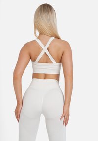 Witte sportbeha met kruisende bandjes, hoogstaande witte leggings met meshnit en een zachte textuur. Eenvoudig en aansluitend ontwerp.