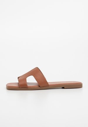 Brun flad klip klip sandal med bred rem med udskæringsdesign og firkantet snude sål på hvid baggrund.