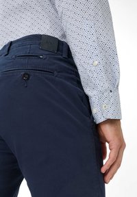 Navyblauwe broek met een gestructureerde afwerking, voorzien van zijzakken en een met knoop afgesloten achterzak. Patroonstrui met kleine blauwe stippen en knopen aan de mouwen.