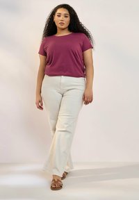 Curvad passform kortärmad skjorta i plommon, kombinerad med vita utsvängda byxor, med detaljerade skor som har utsmyckningar. Slät tygtextur.