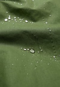 Tissu vert résistant à l'eau avec une texture lisse, présentant de petites gouttes d'eau se rassemblant à la surface et des détails de couture subtils.