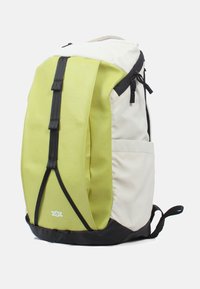 Rugzak in een twee-kleurig ontwerp: lichtbeige lichaam en felgroene zijpaneel. Voorzien van zwarte riemen en accenten, en een ritsluiting.