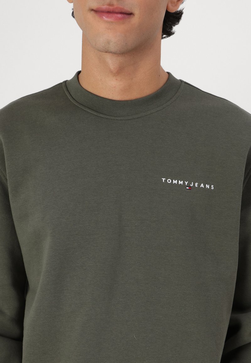 Felpa verde scuro in cotone, con scollatura a girocollo, polsini a costine e un piccolo logo "TOMMY JEANS" bianco sul petto.