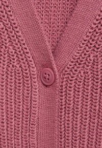 Pleteni kardigan v mehki roza barvi, ki ima V-izrez, rebrasto teksturo in okroglo zaponko spredaj.